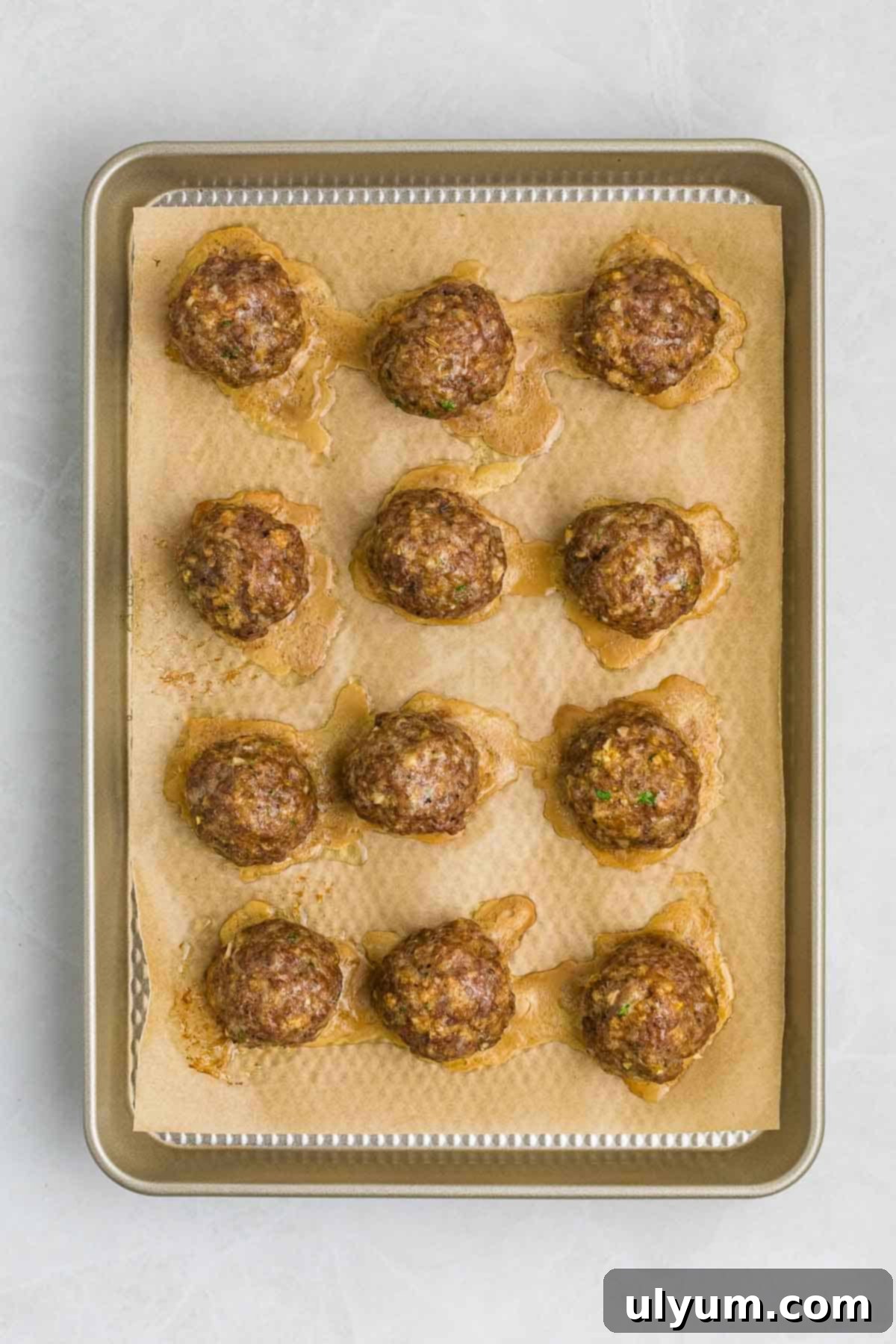 A baking sheet with cooked meatballs on parchment paper.