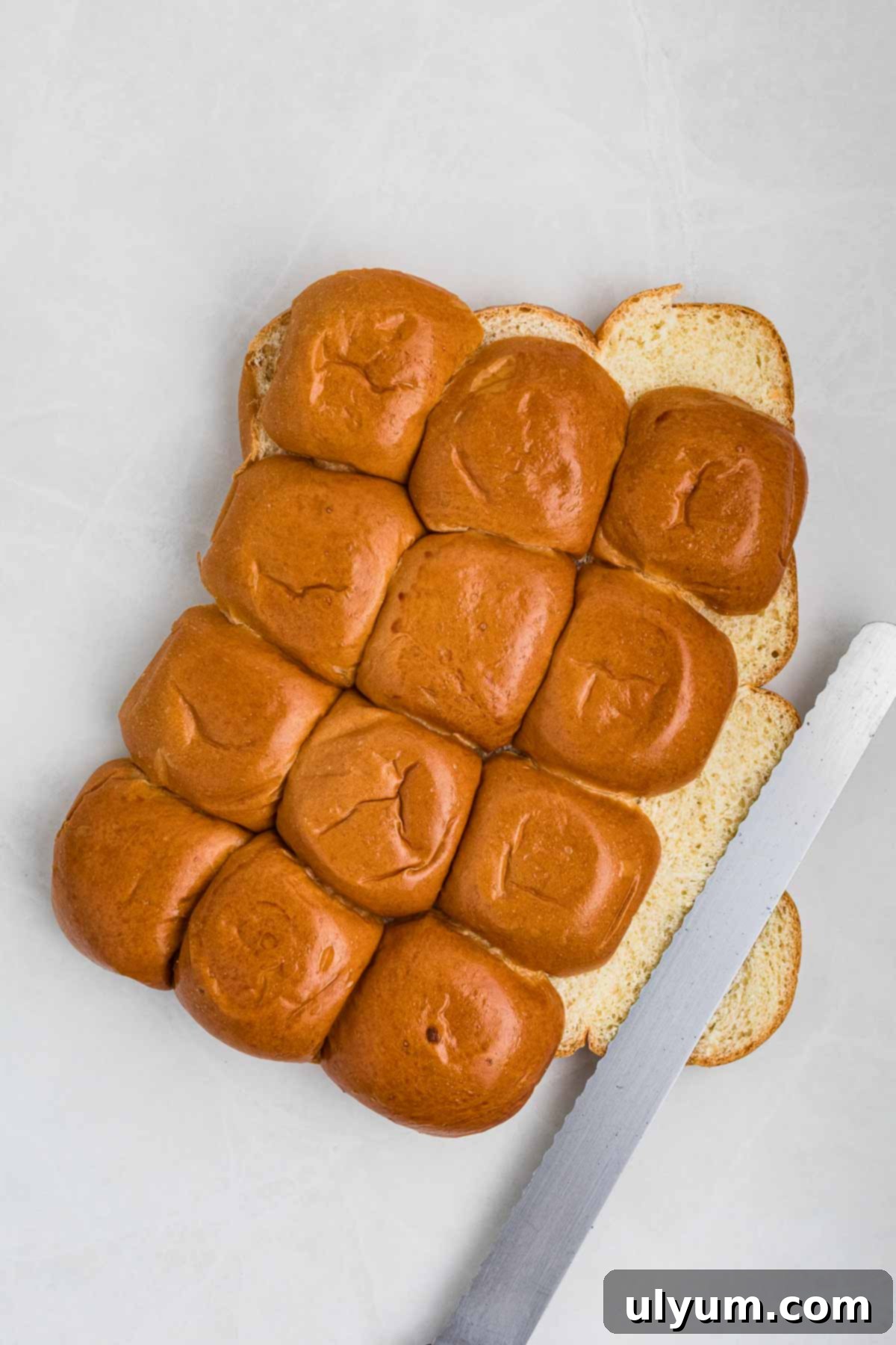 A bread knife next to sliced Hawaiian rolls cut horizontally.