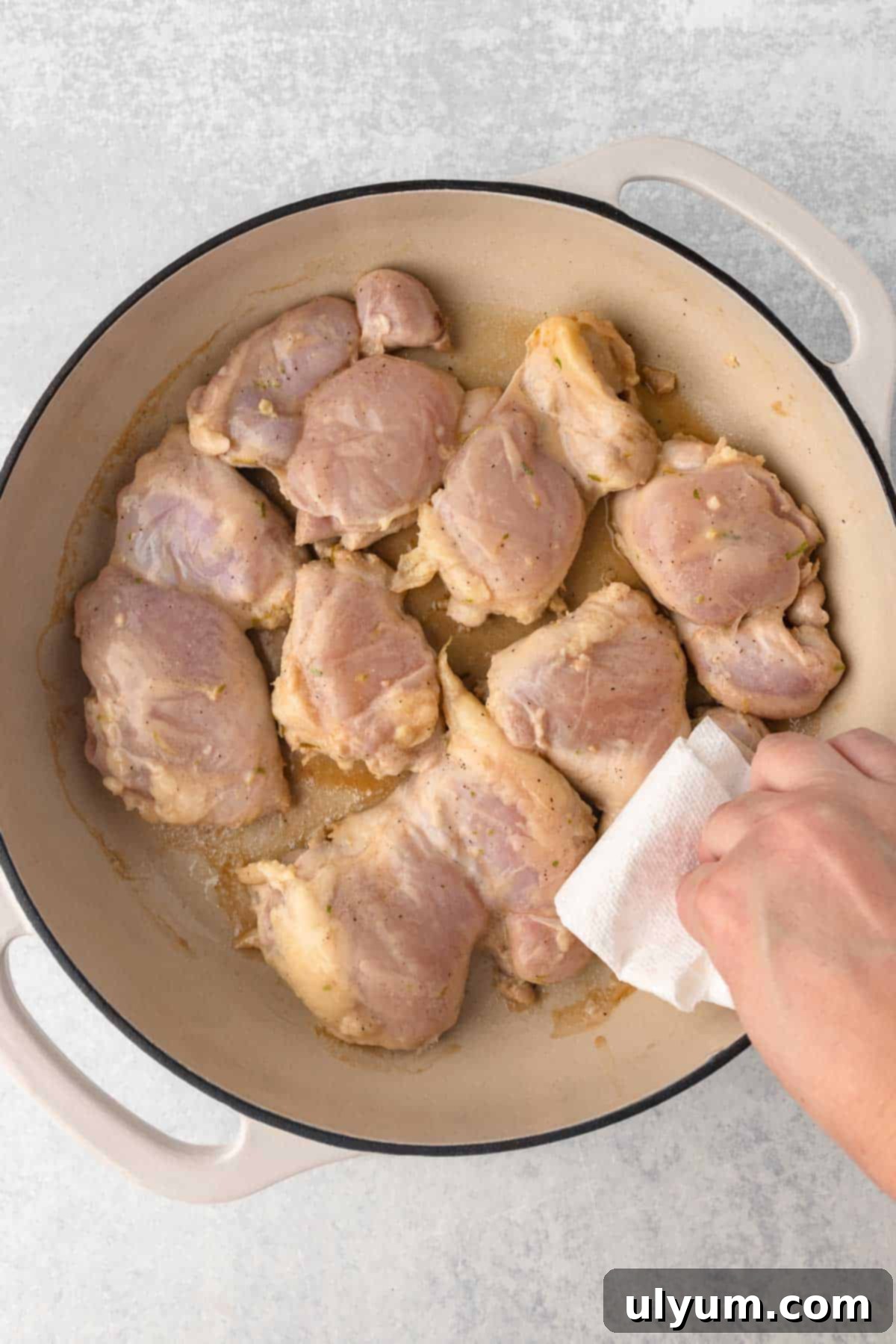 Easy One Pan Coconut Lime Chicken 6 Raw marinated chicken thighs arranged in a large pan being blotted dry with a paper towel.