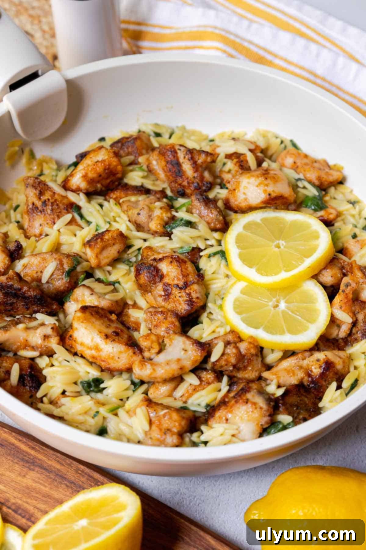 Bright Lemon Chicken Orzo Skillet 2 Seasoned diced chicken thighs in a large skillet with orzo, spinach, and lemon slices.