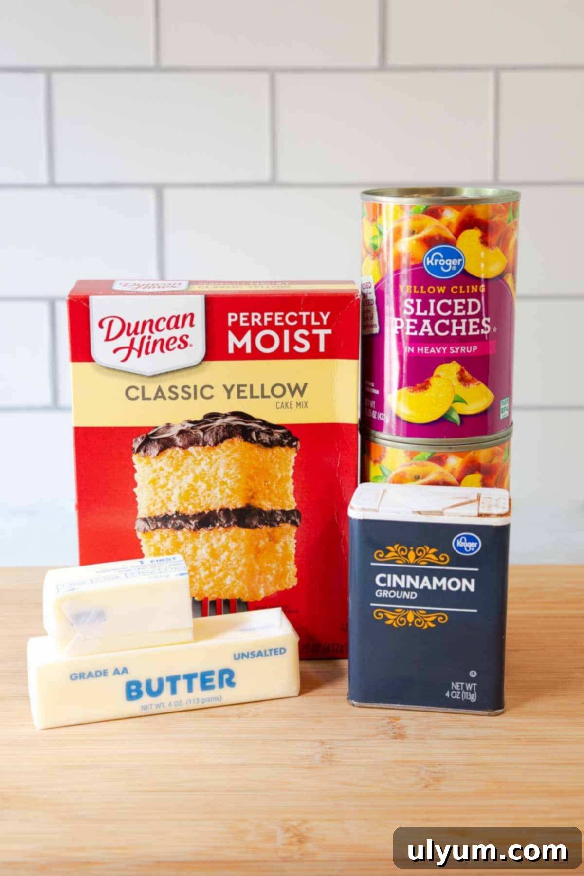Box of yellow cake mix, two cans of sliced peaches, ground cinnamon, and two sticks of butter.