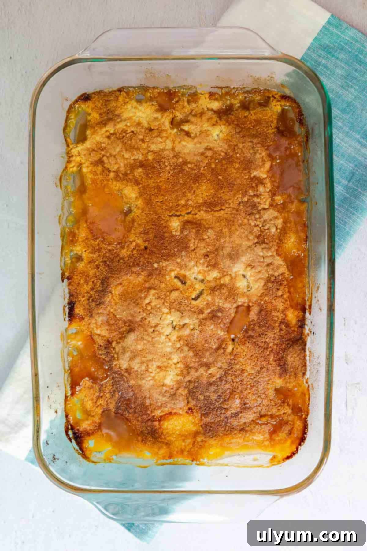 A baked peach cobbler with a golden brown top in a glass dish.