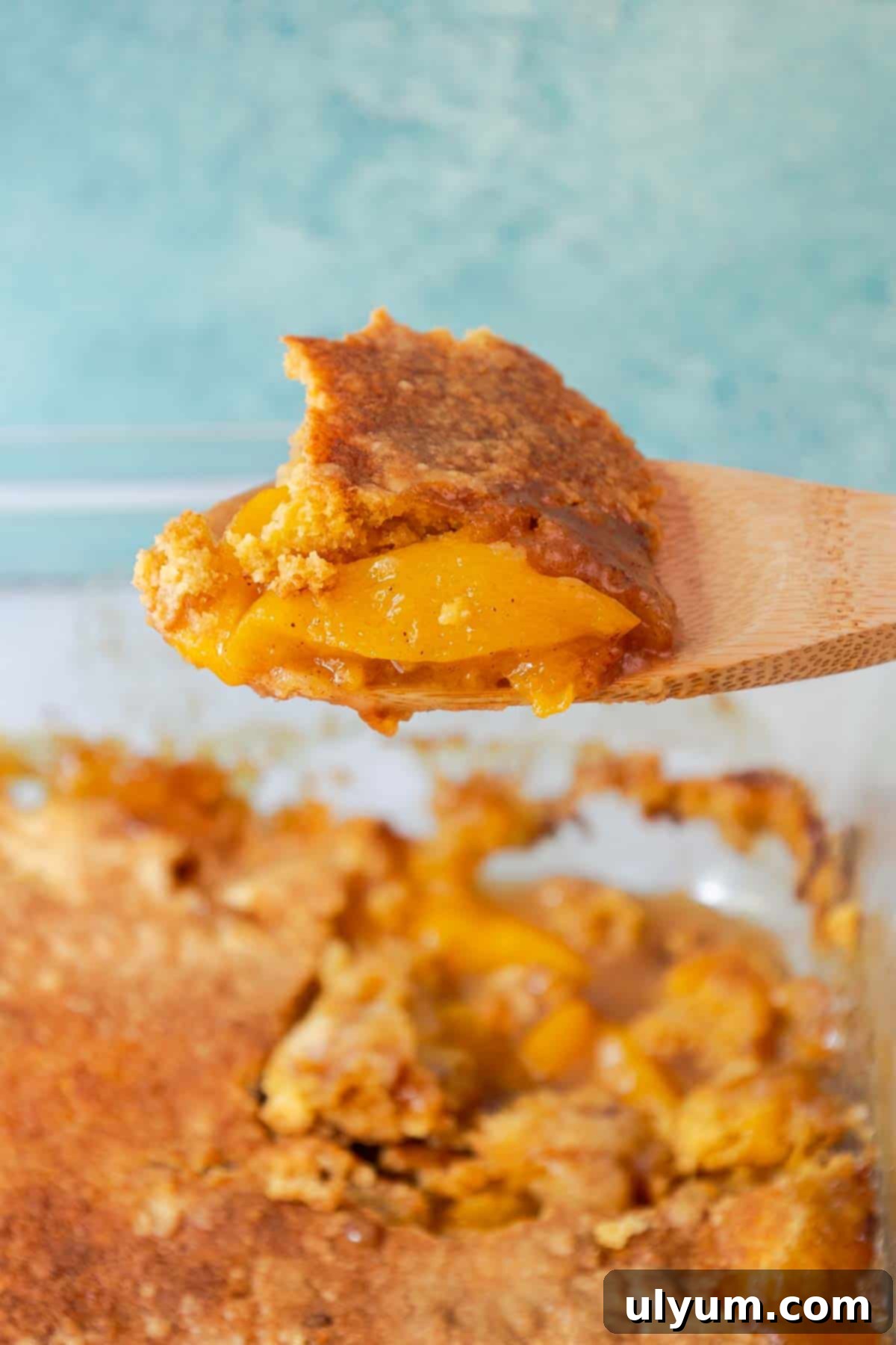 A wooden spoon holding a scoop of peach cobbler.