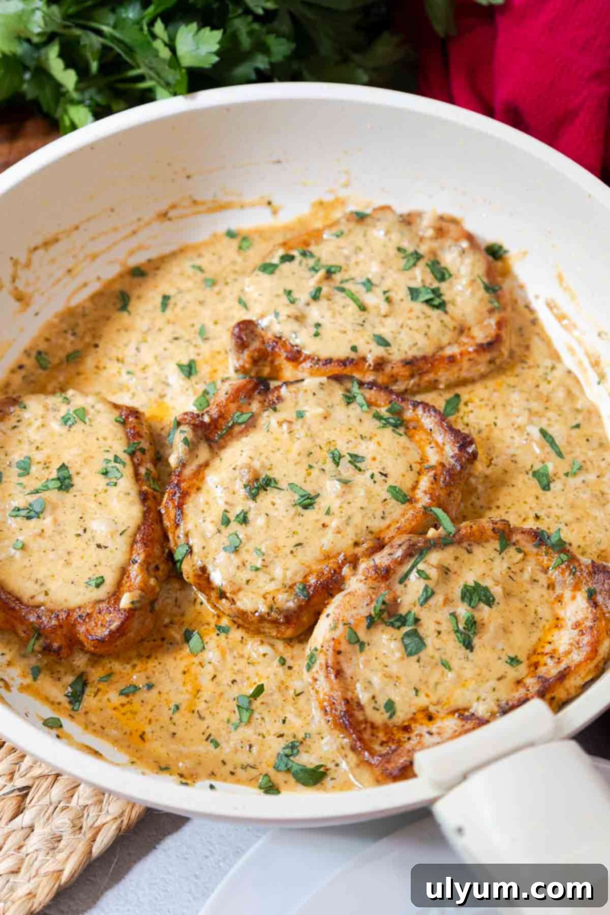 Four pork chops in a skillet covered with creamy garlic sauce and fresh parsley.