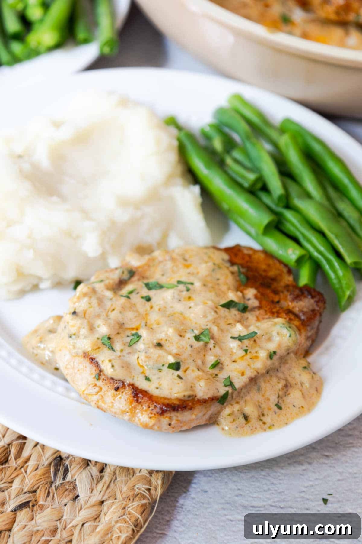 Pork chop smothered in garlic cream sauce next to mashed potatoes and green beans.