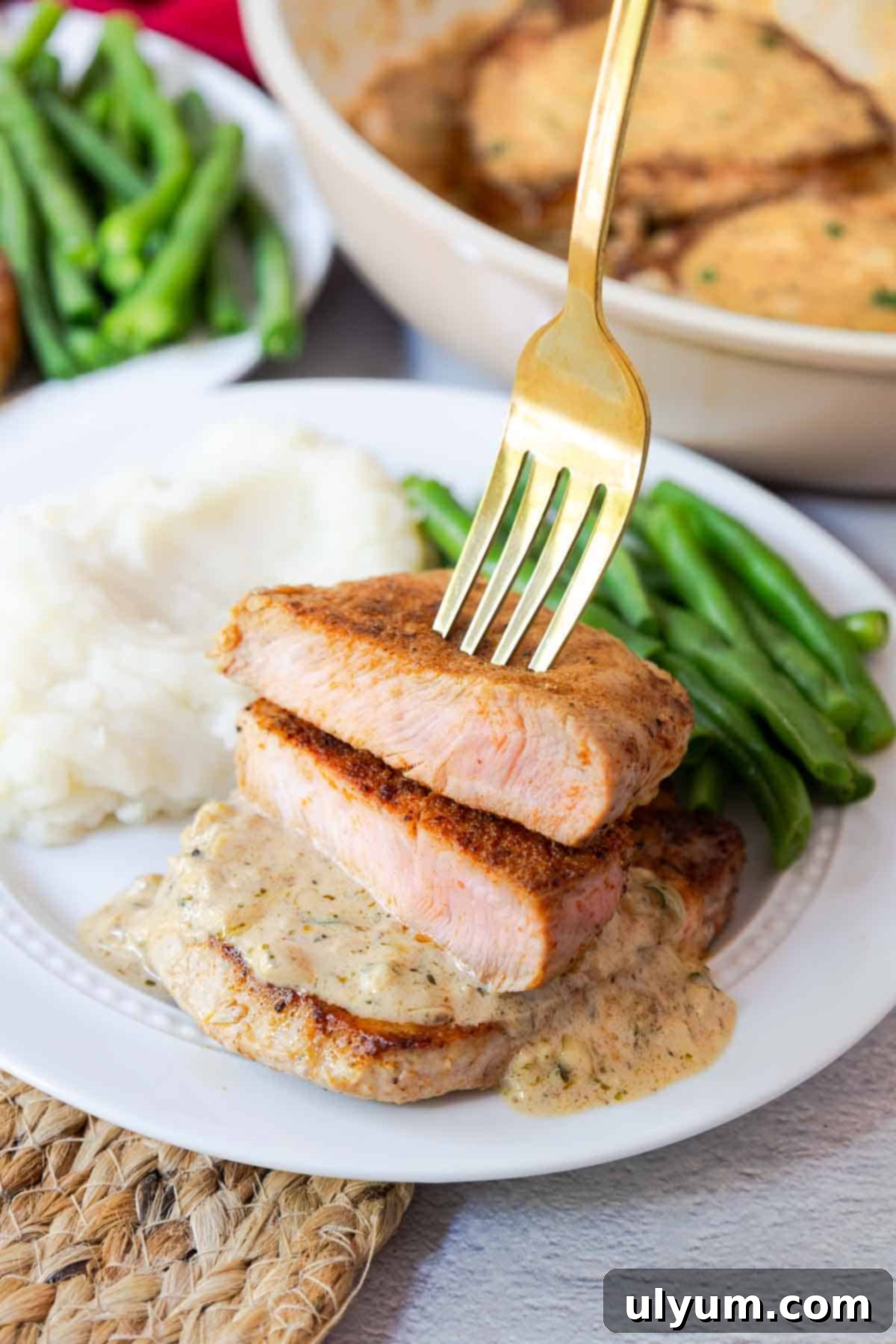 Sliced pork chop with a pink center on a plate with sauce, mashed potatoes, and green beans.