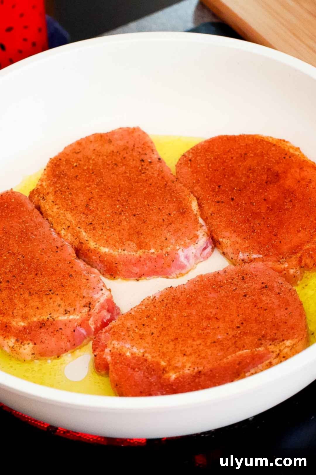 Seasoned pork chops in a skillet with hot oil.
