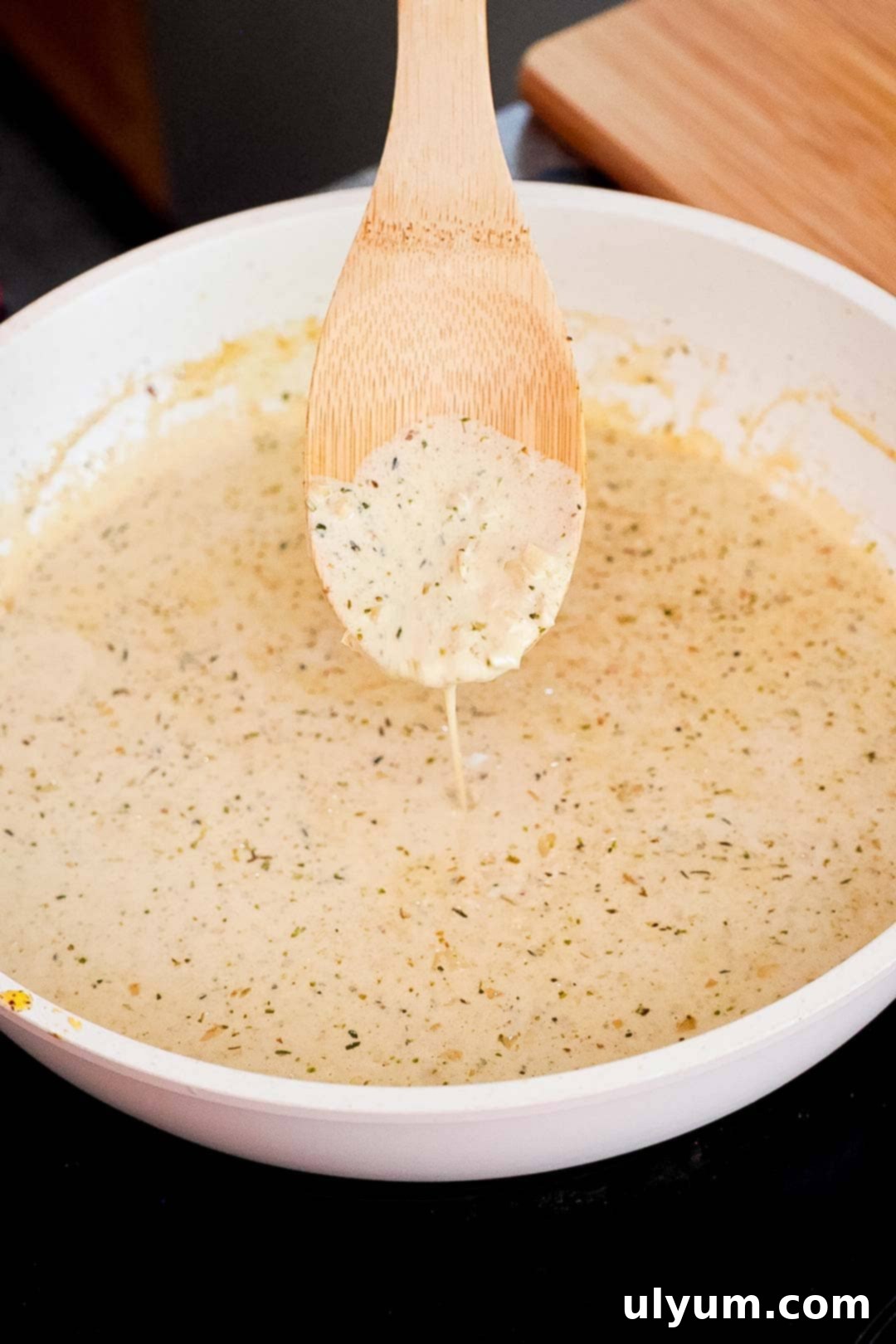 Creamy sauce in a skillet with a wooden spoon holding a spoonful.