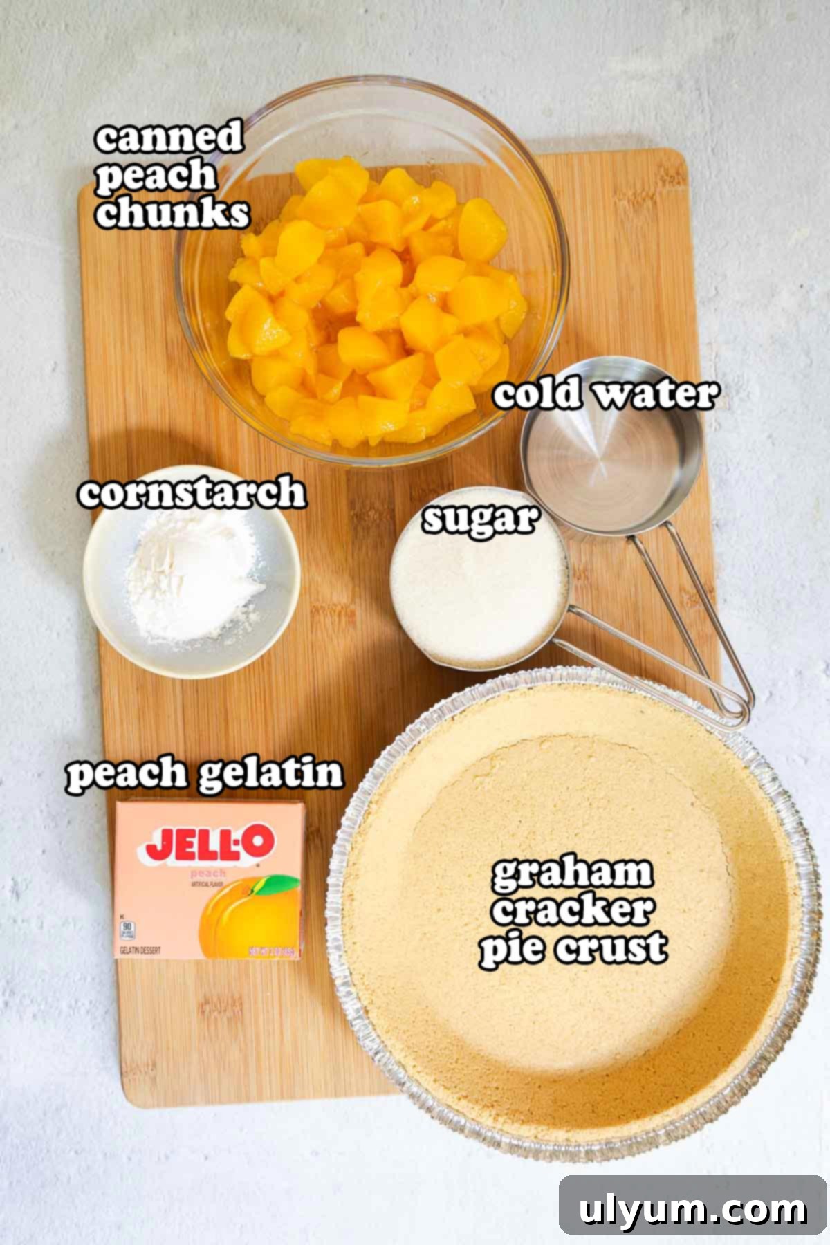 Ingredients for peach Jello pie laid out: canned peach chunks, cold water, cornstarch, sugar, peach gelatin, and a graham cracker pie crust.