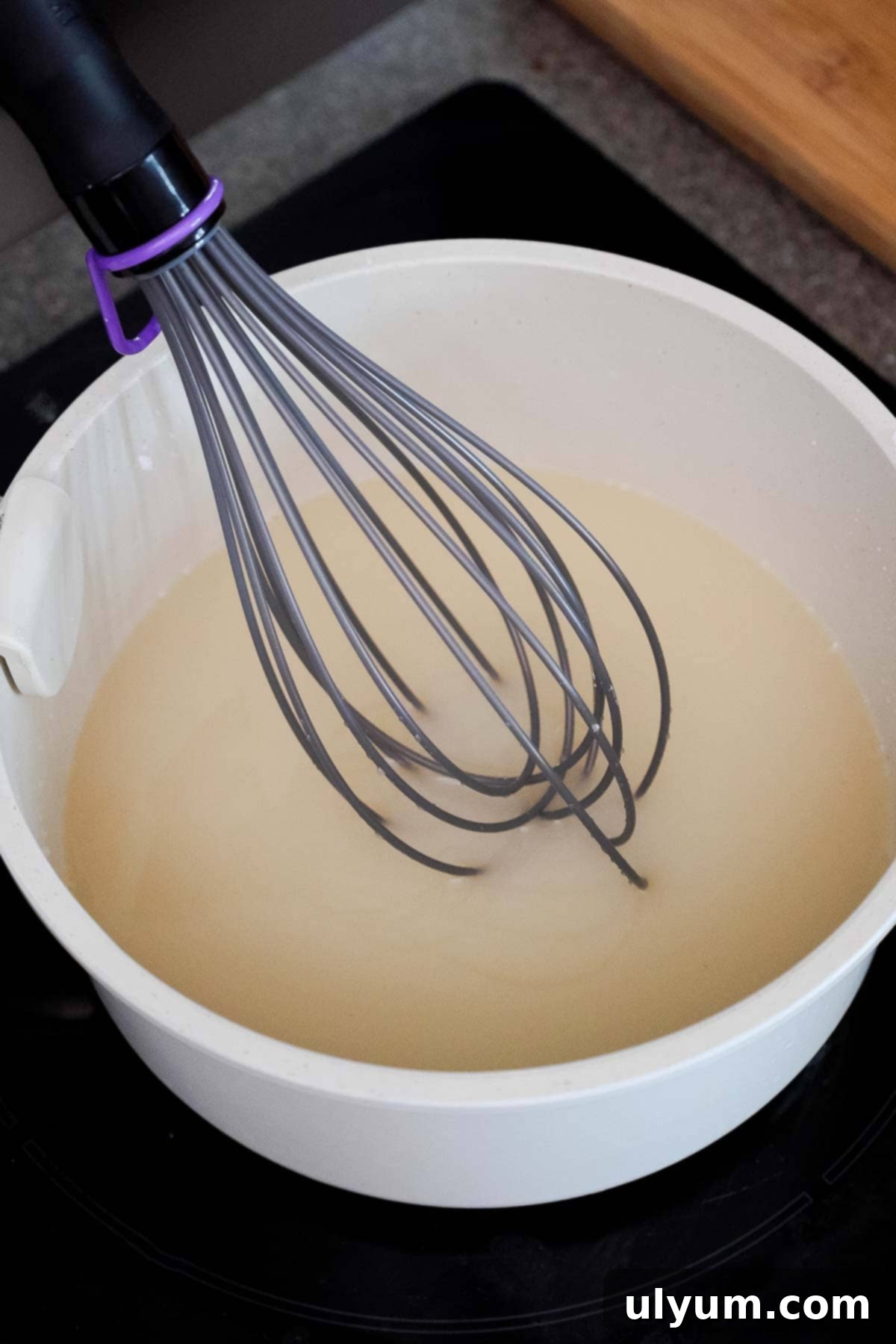 A saucepan with a whisk stirring cold water, sugar, and cornstarch together until dissolved.