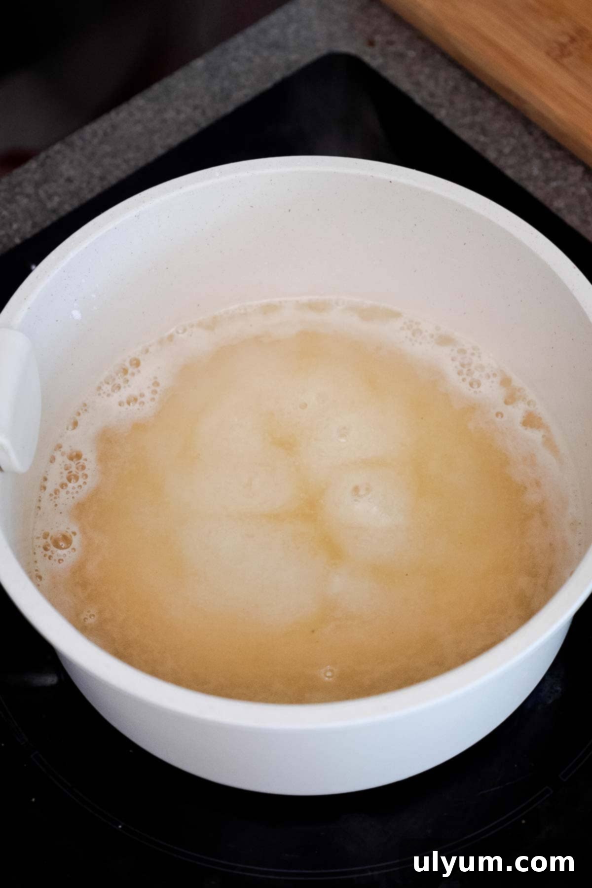 A white pot with a bubbling pale liquid, the sugar and cornstarch mixture thickening.