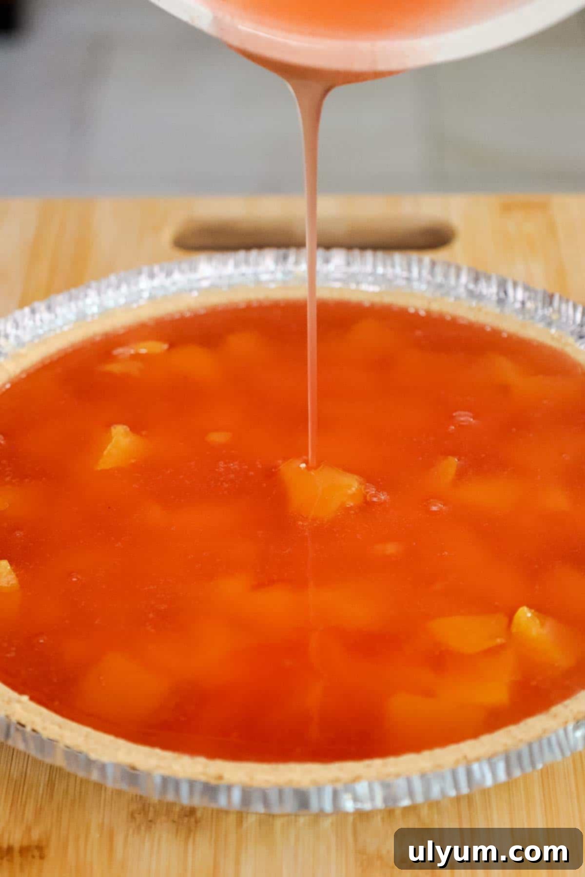 Cooled peach gelatin mixture being carefully poured over the peaches in the pie crust.