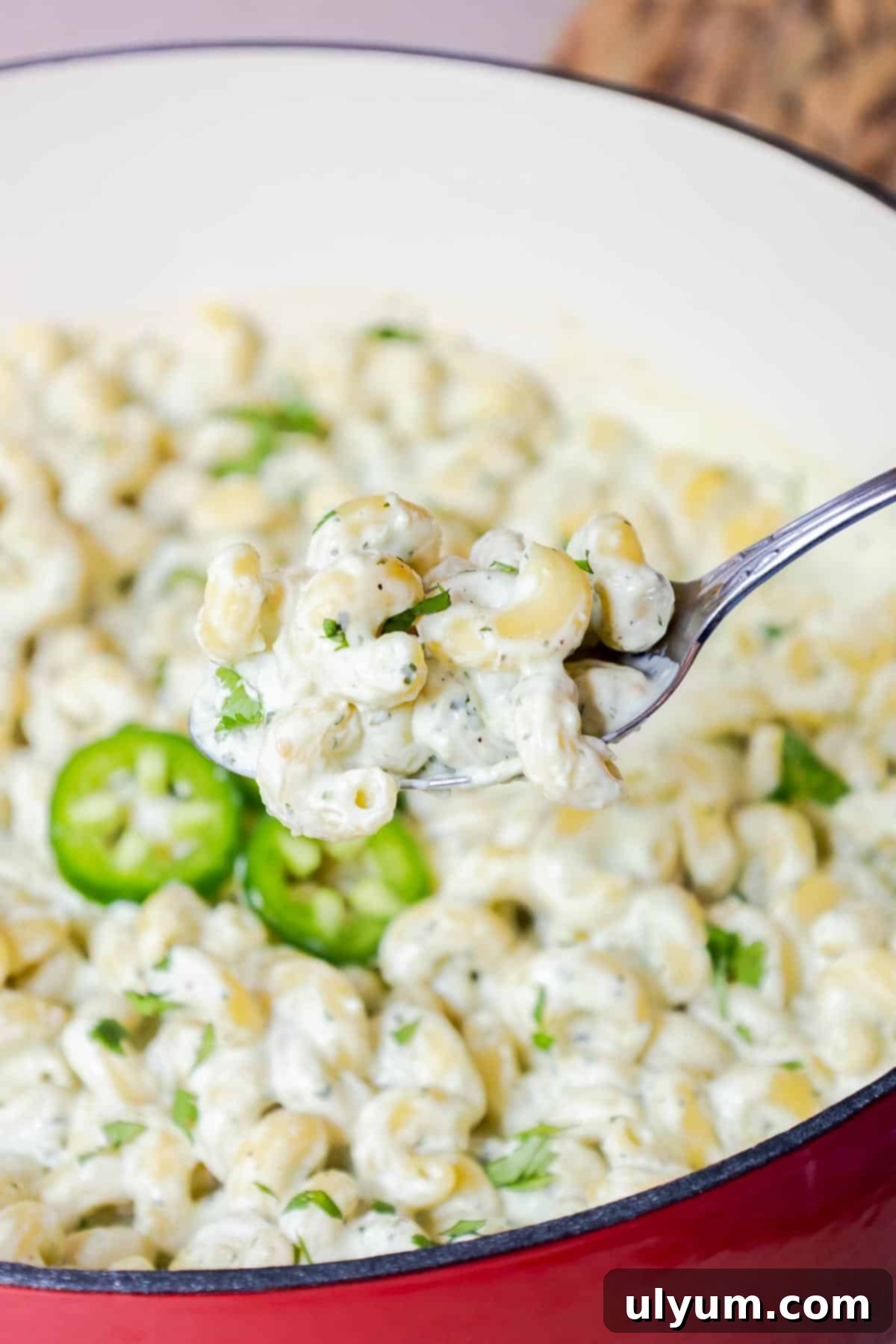 Spicy Creamy Jalapeño Ranch Pasta 11 A spoon lifting creamy pasta from a pot with jalapeños and cilantro.