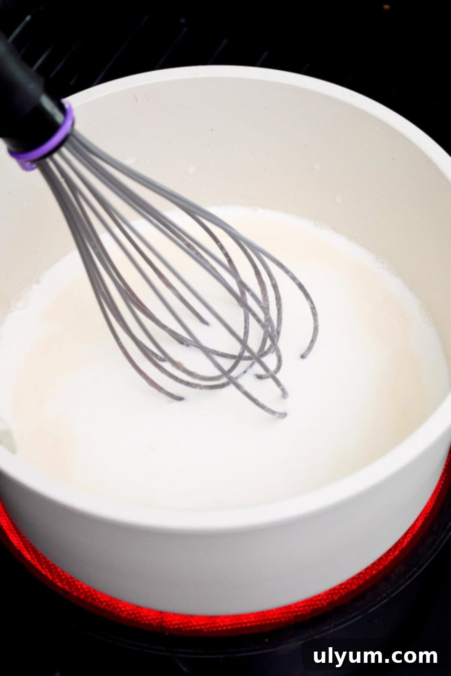 A whisk mixing half and half into the butter and flour roux, gradually creating a smooth, creamy base for the cheese sauce.