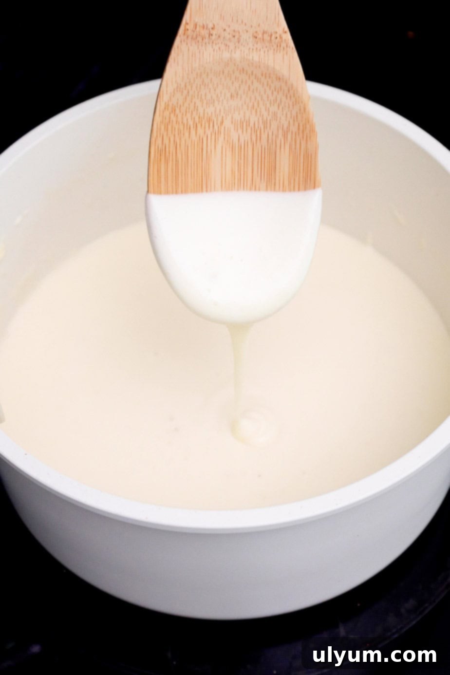 A spoon lifting a thick, velvety cheese sauce from a pot, showing its creamy consistency.
