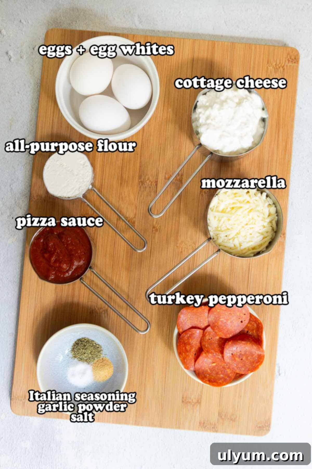 Ingredients for cottage cheese pizza crust arranged on a cutting board, including cottage cheese, eggs, flour, seasonings, pizza sauce, mozzarella, and turkey pepperoni.