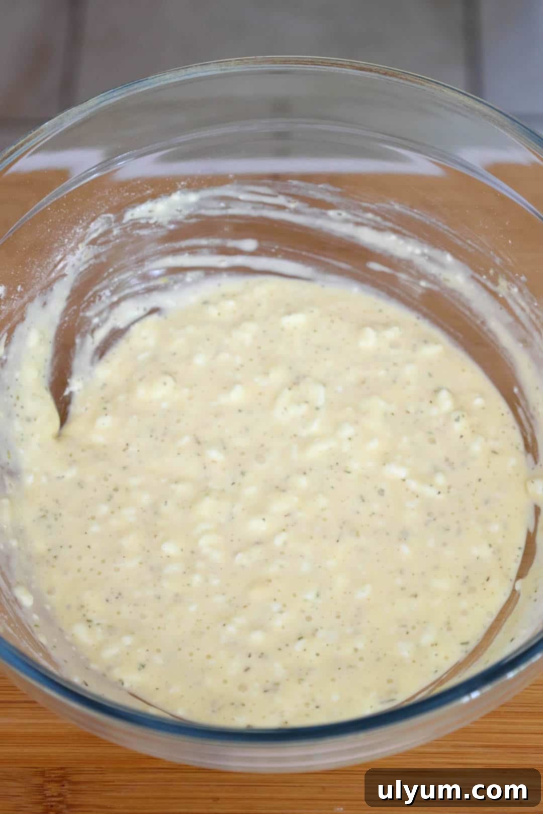 A glass bowl containing the uncooked pizza crust batter, a smooth mixture of cottage cheese, eggs, flour, and seasonings.
