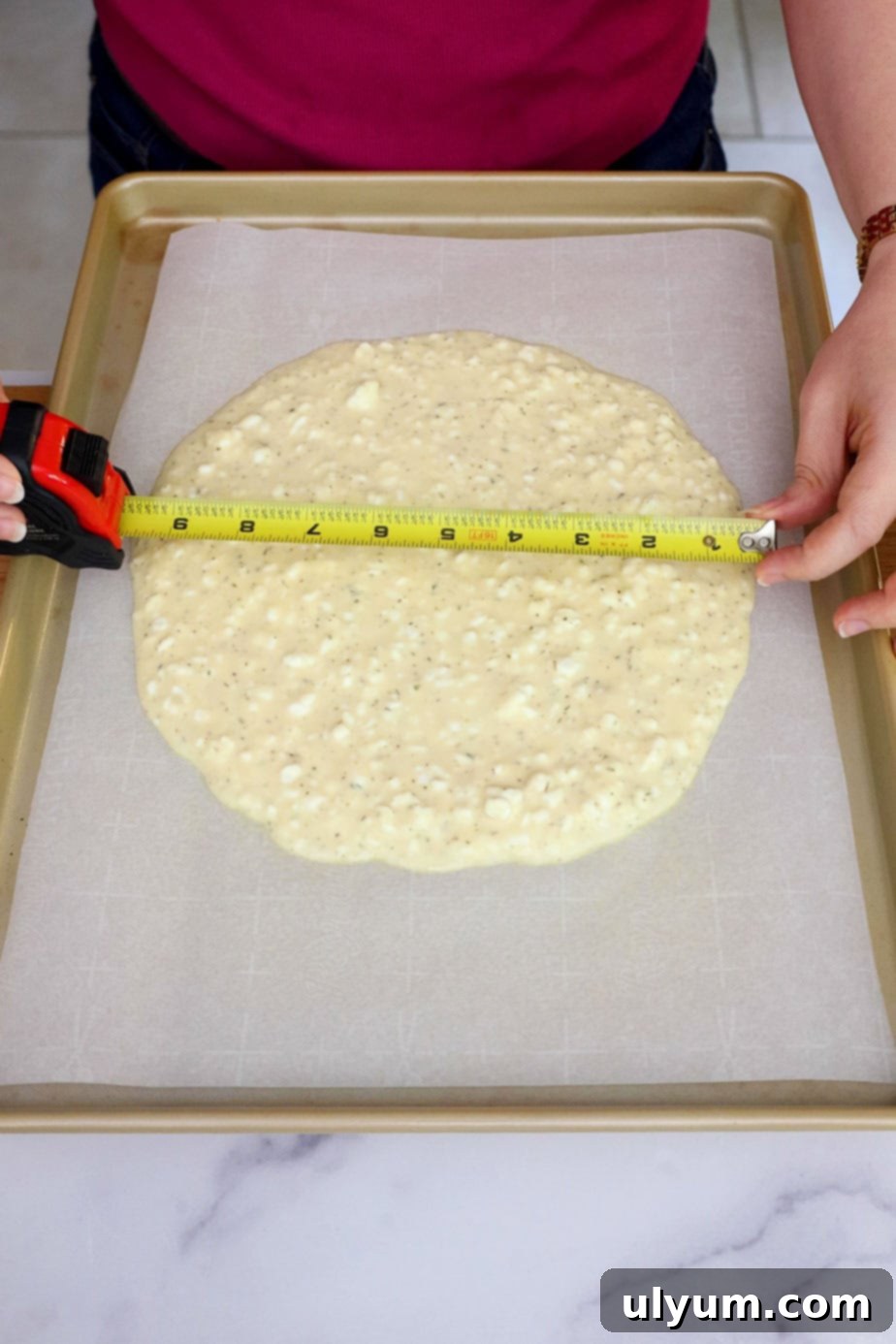 Cottage cheese pizza batter spread into a perfect 10-inch circle on parchment paper with a tape measure confirming the diameter.