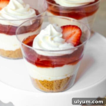 Strawberry cheesecake cups with graham cracker crust, cream filling, strawberry jam, and whipped topping with a strawberry slice, ready to be enjoyed.
