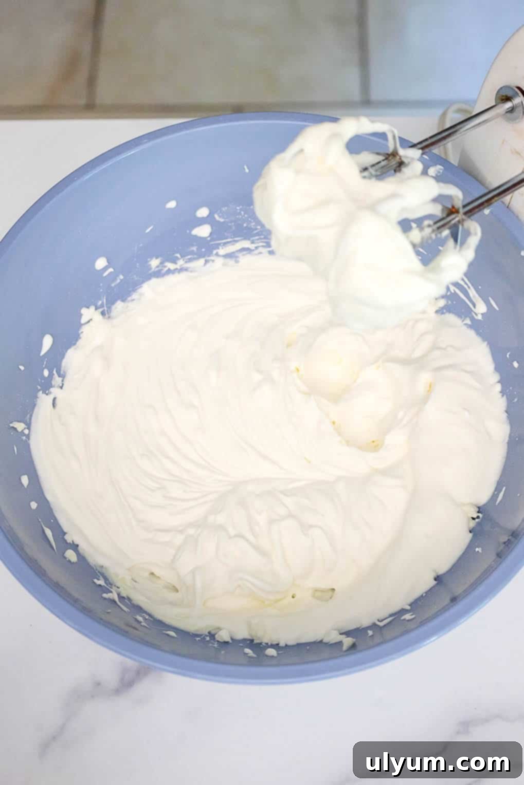 Whipped cheesecake filling in a large mixing bowl with electric beaters resting inside, ready for assembly.