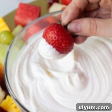 A hand holding a fresh strawberry dipped in fluffy marshmallow fruit dip.