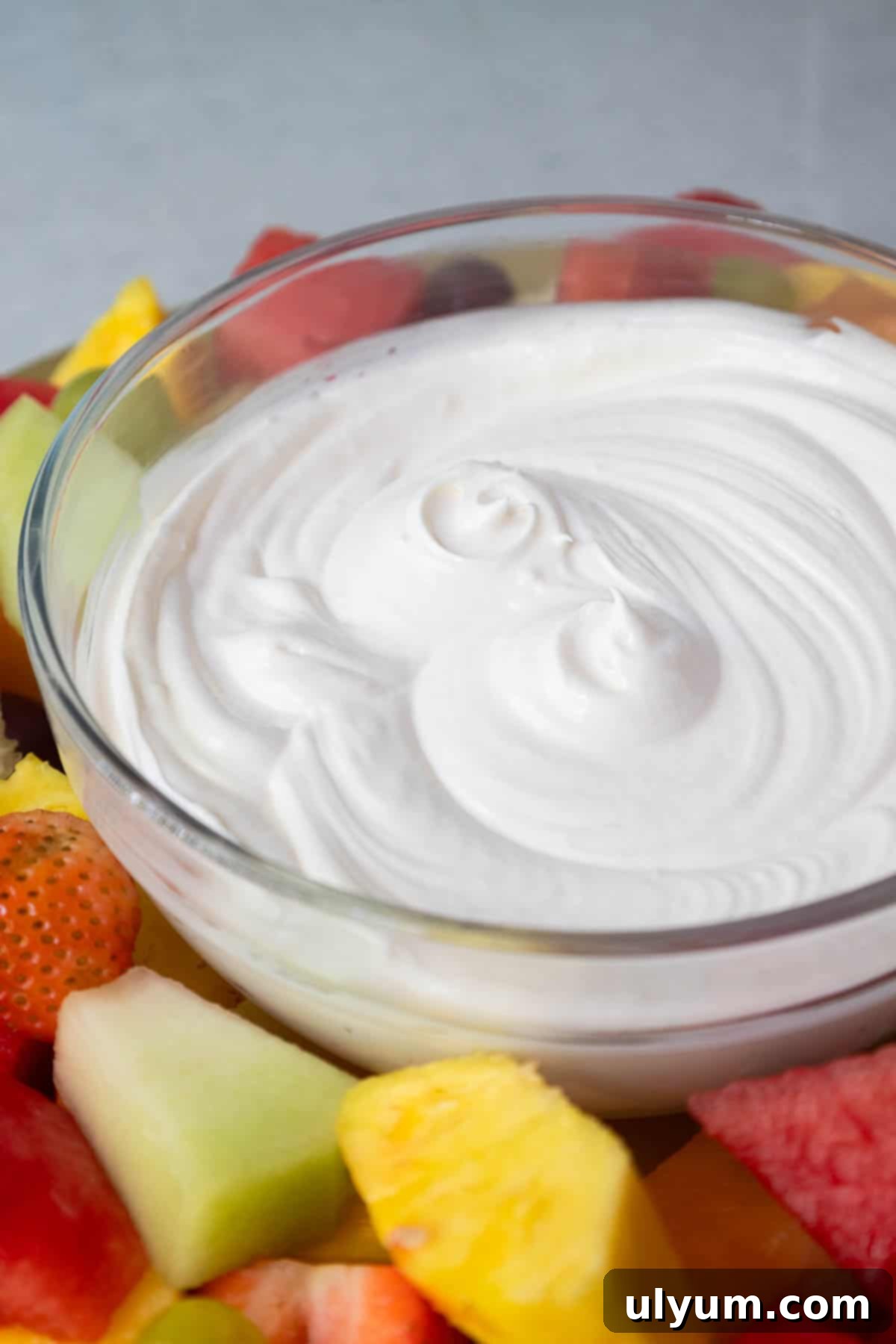 Close-up of a swirled bowl of white fruit dip surrounded by colorful chunks of fresh fruit.