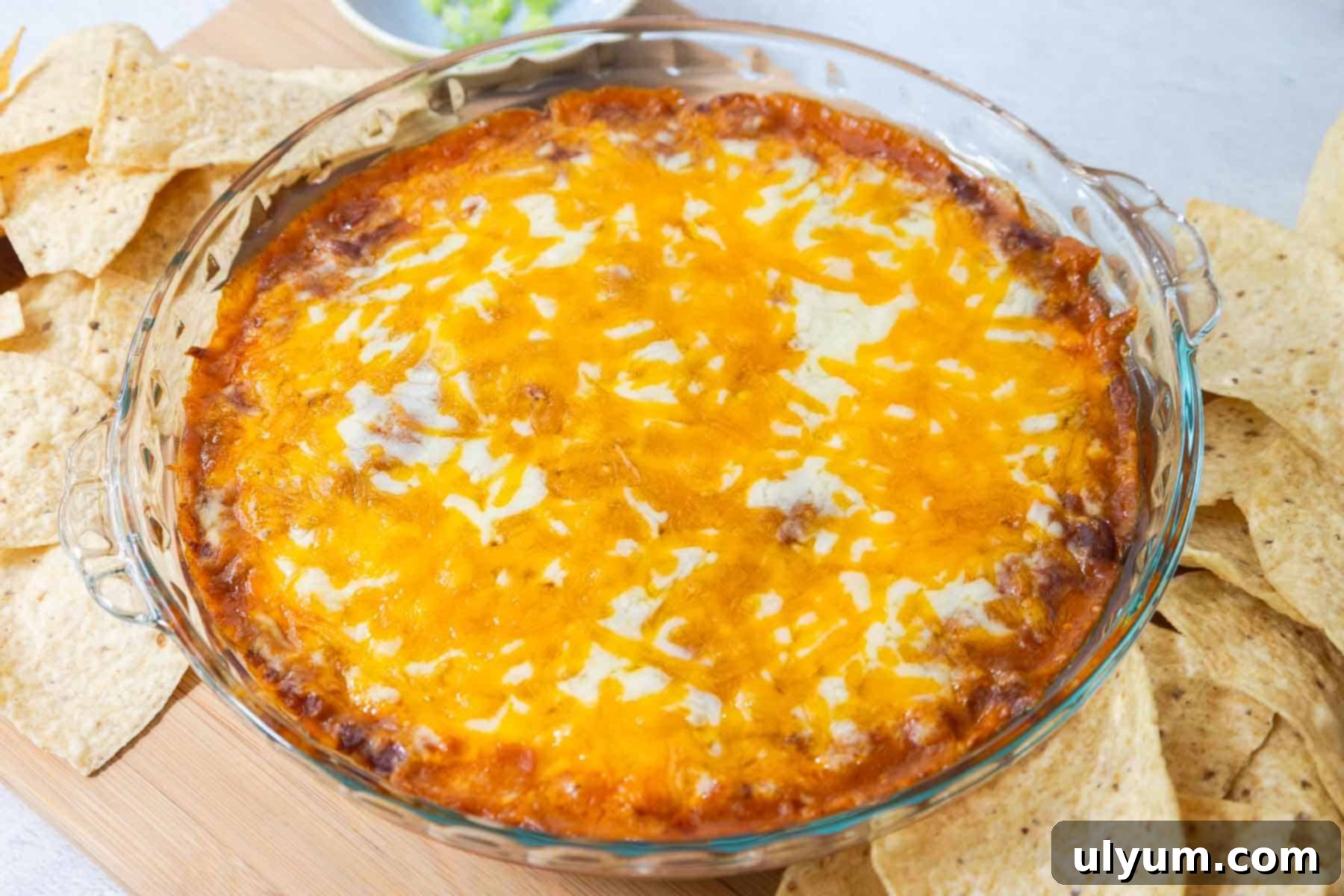 Freshly baked chili cheese dip with golden, bubbly melted cheese on top, placed next to tortilla chips for dipping.