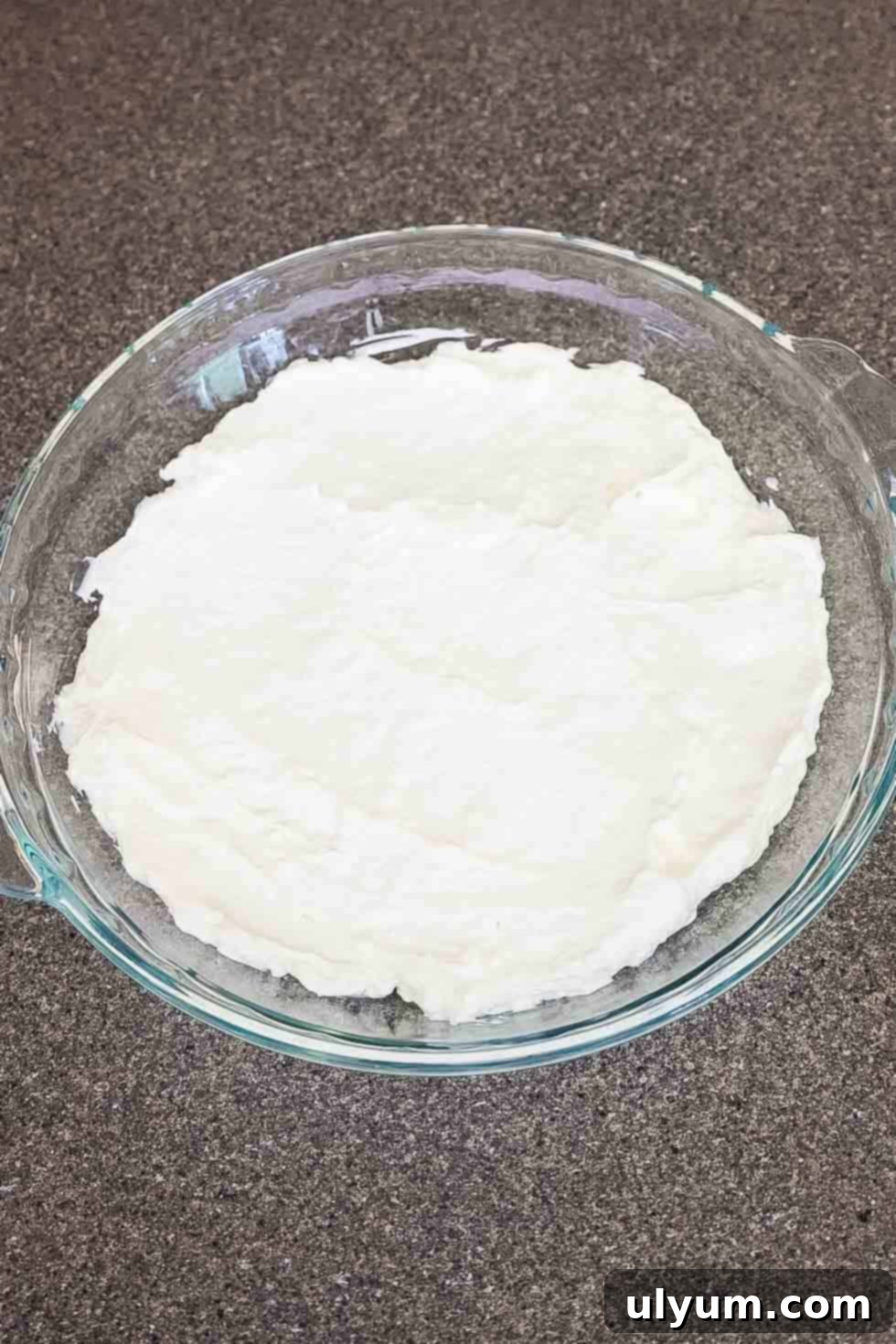 A glass baking dish with the creamy white base layer of the dip spread evenly across the bottom.