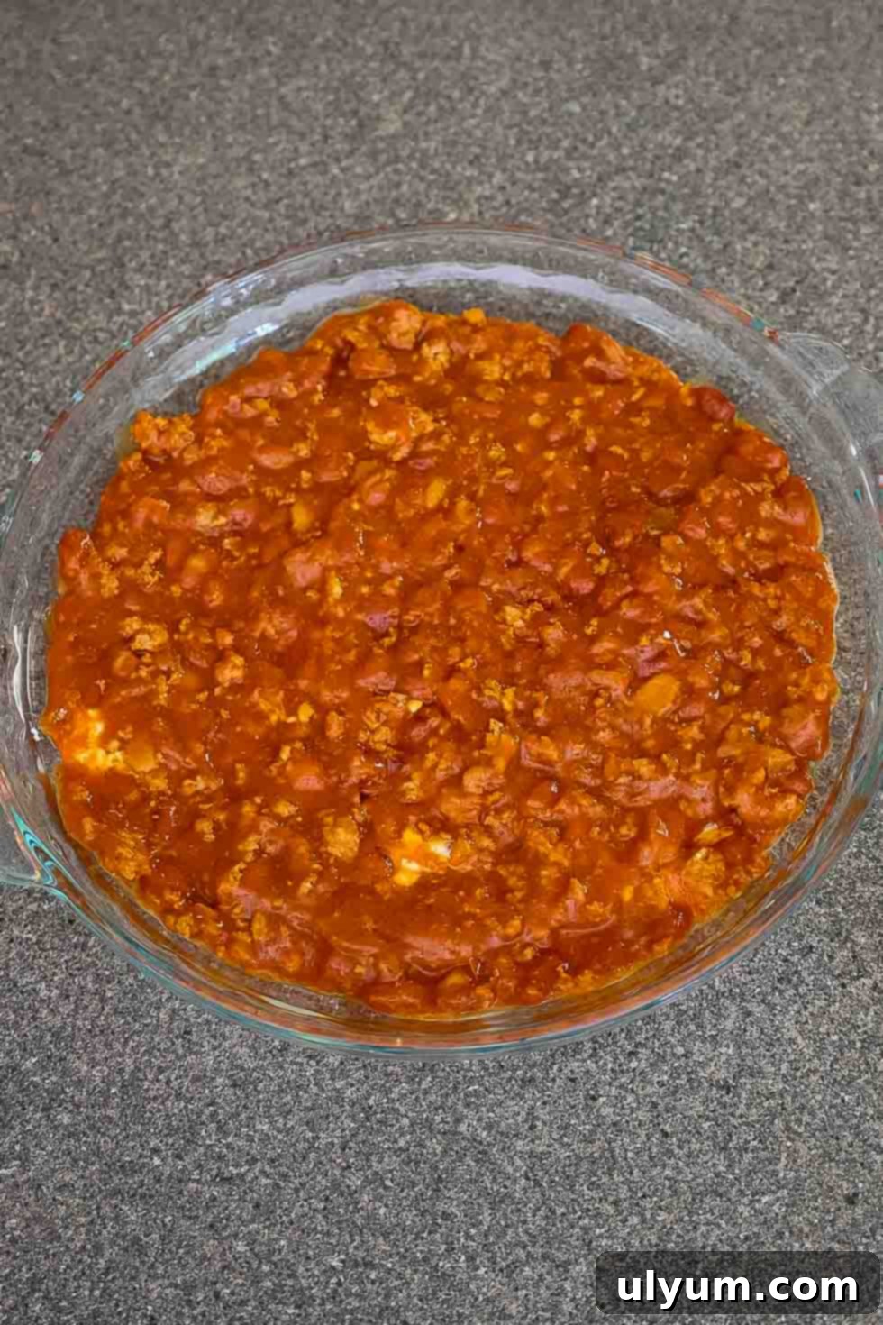 The second layer of the dip made with canned chili spread over the cream cheese mixture in a glass baking dish.