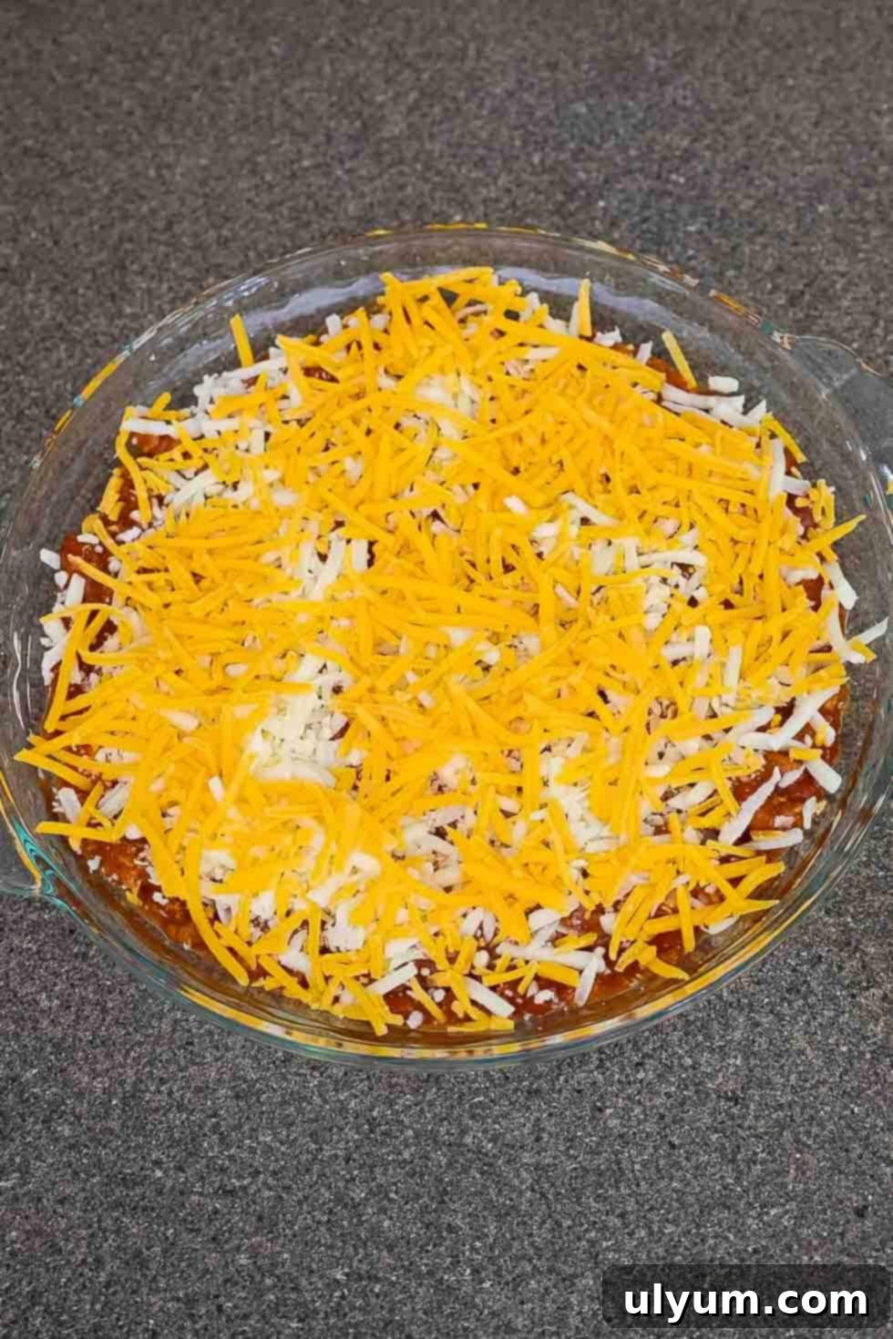 Unbaked chili cheese dip topped with a generous amount of shredded cheddar and mozzarella cheeses.