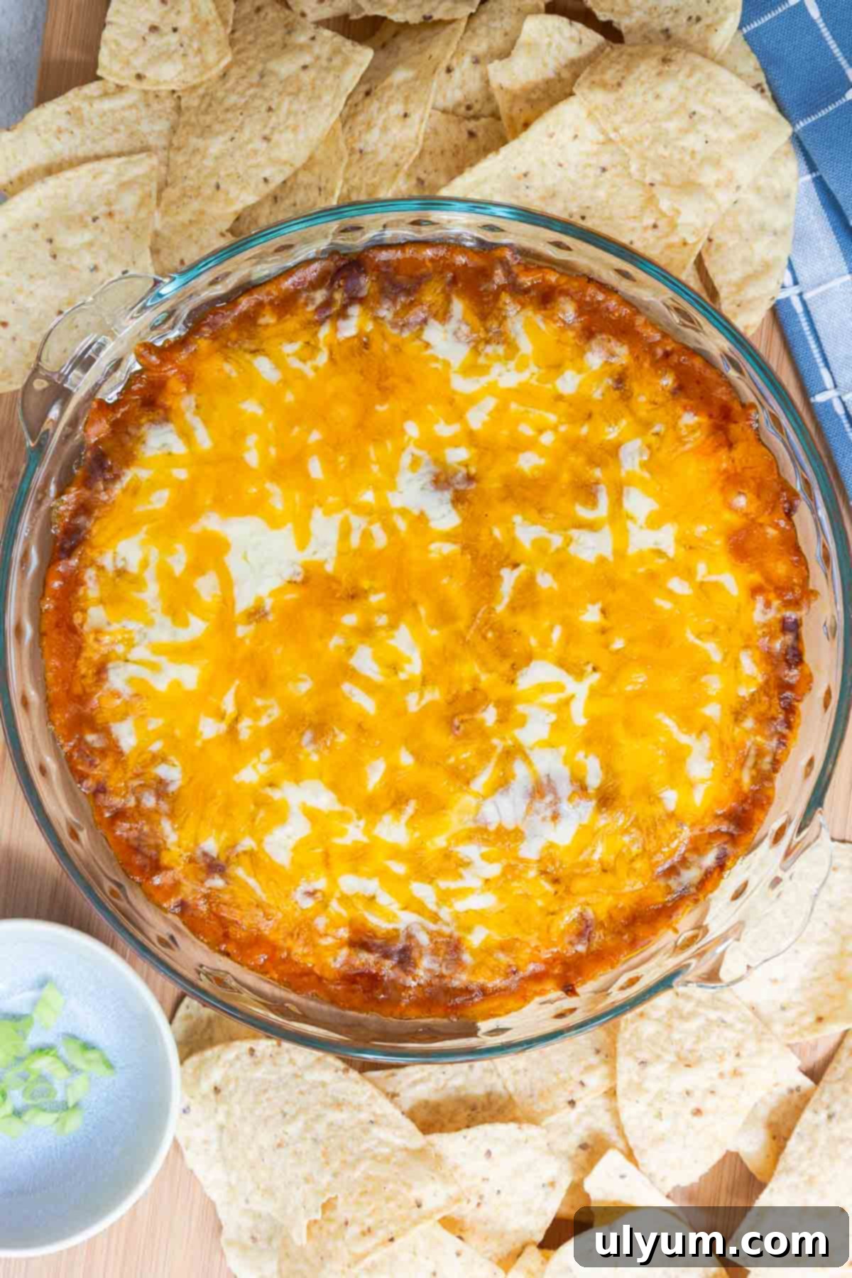 Top-down view of baked chili cheese dip surrounded by tortilla chips, with a bowl of green onions off to the side for garnish.