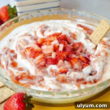 Strawberry cheesecake dip topped with swirled strawberry jam and diced fresh strawberries served in a glass pie dish.