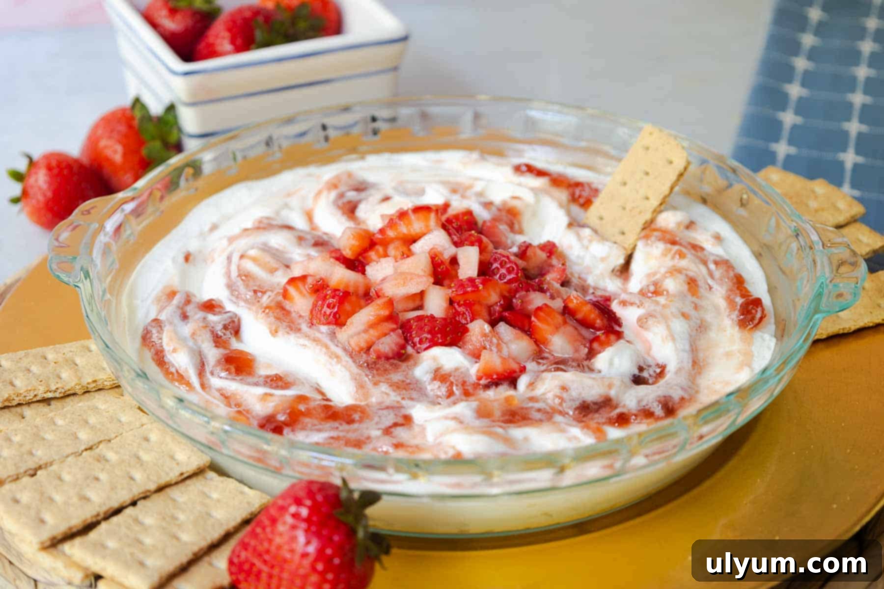Atrawberry cheesecake dip in a glass pie dish, surrounded by graham crackers and fresh strawberries.