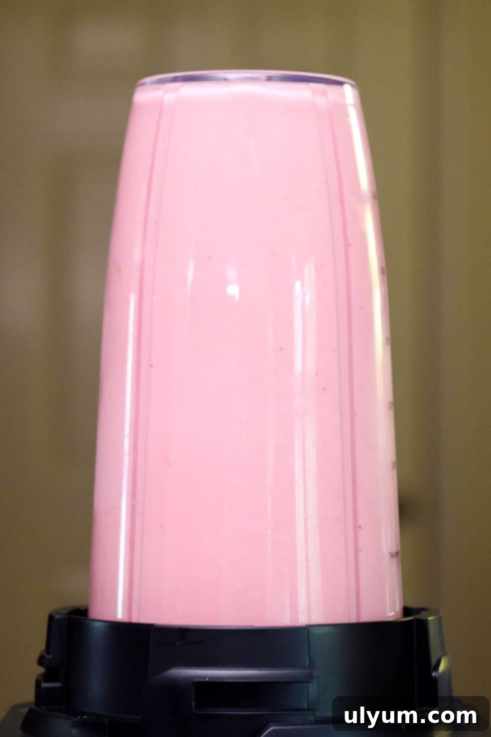 A pink strawberry smoothie blending in a clear blender cup.