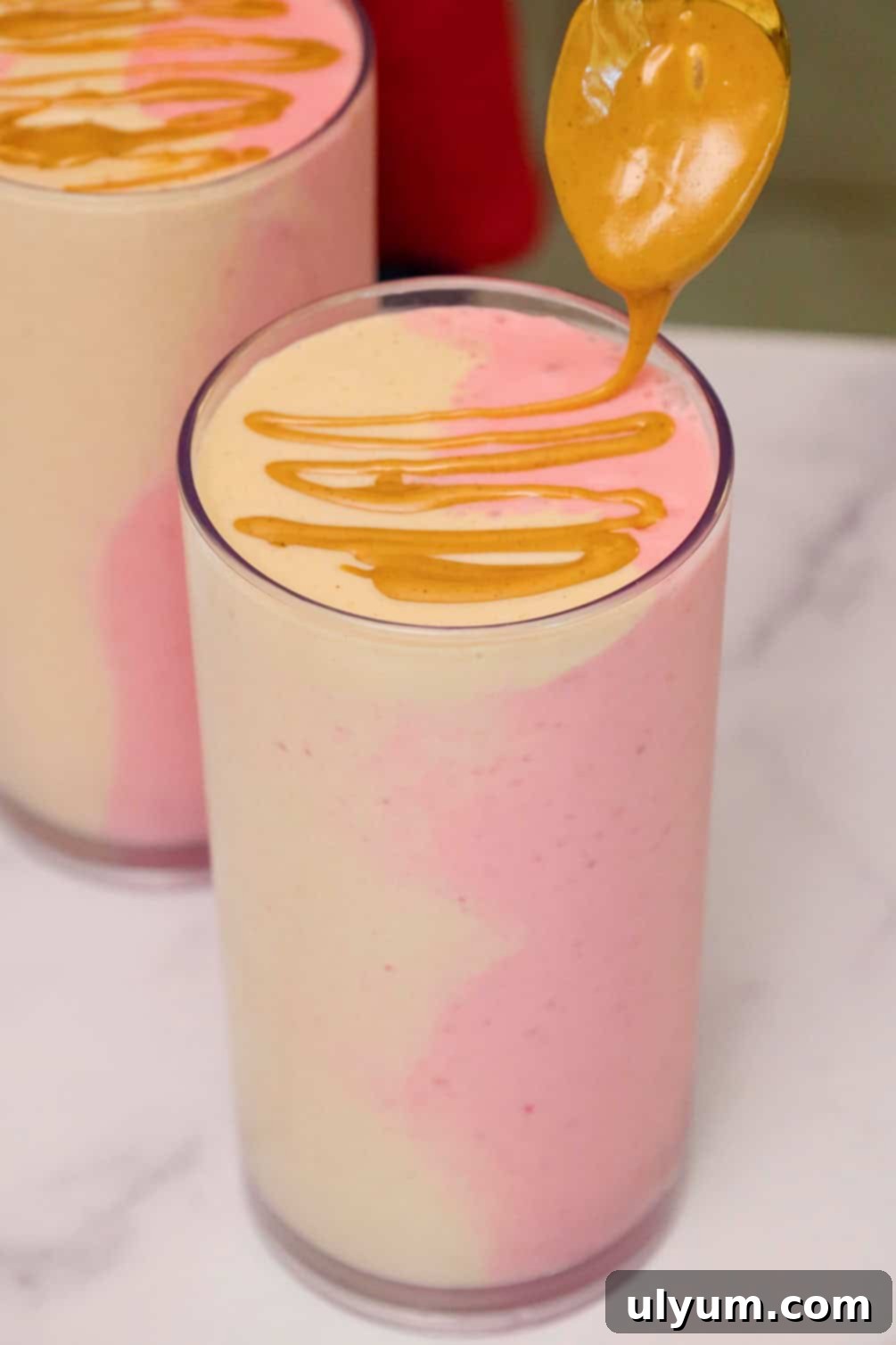 Peanut butter being drizzled over the top of a finished swirled peanut butter and jelly smoothie in a glass.