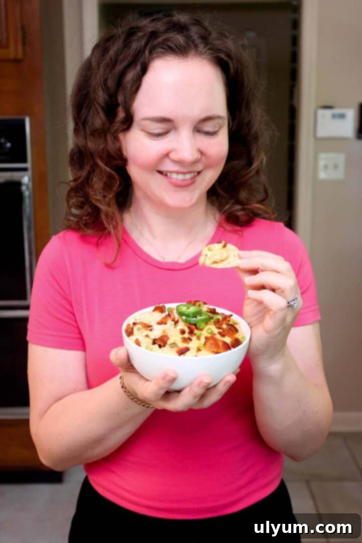 Kelsey Smith holding a bowl of jalapeño popper dip and looking at a chip scooped into the dip.