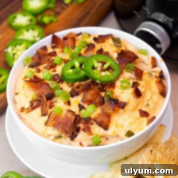 Small bowl of creamy crockpot jalapeño popper dip topped with crispy bacon, sliced jalapeños, and green onions.