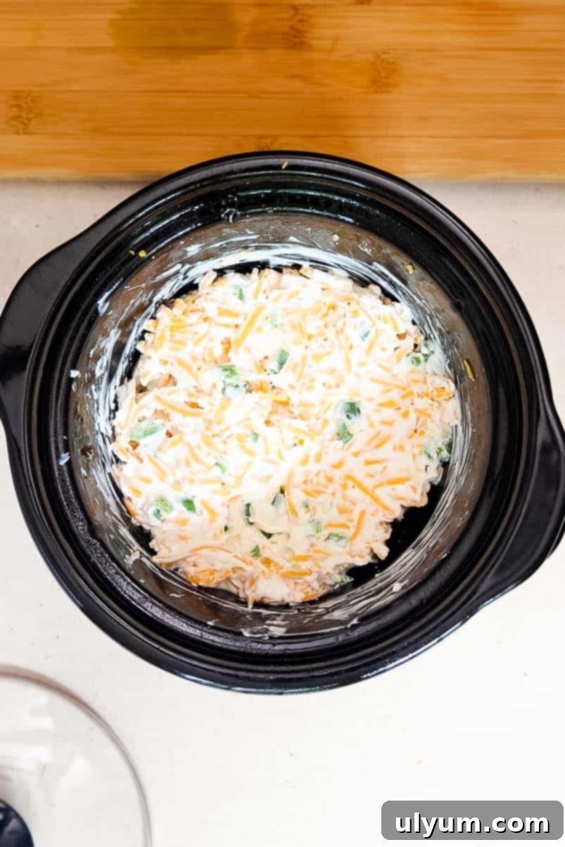 Softened cream cheese, sour cream, garlic powder, diced jalapeños, and shredded cheddar mixed together in a small Crockpot.