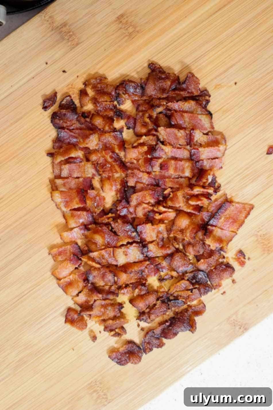 Chopped crispy bacon pieces on a wooden cutting board.