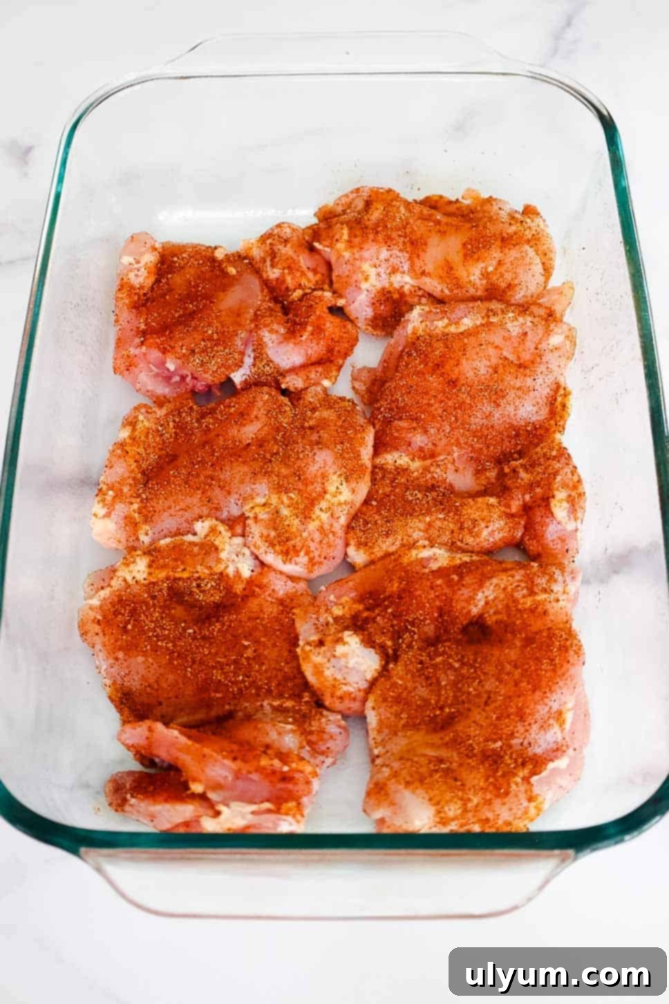 Mouthwatering Oven Baked BBQ Boneless Chicken Thighs 4 Raw boneless chicken thighs evenly coated in dry spice rub, arranged in a glass baking dish before cooking.