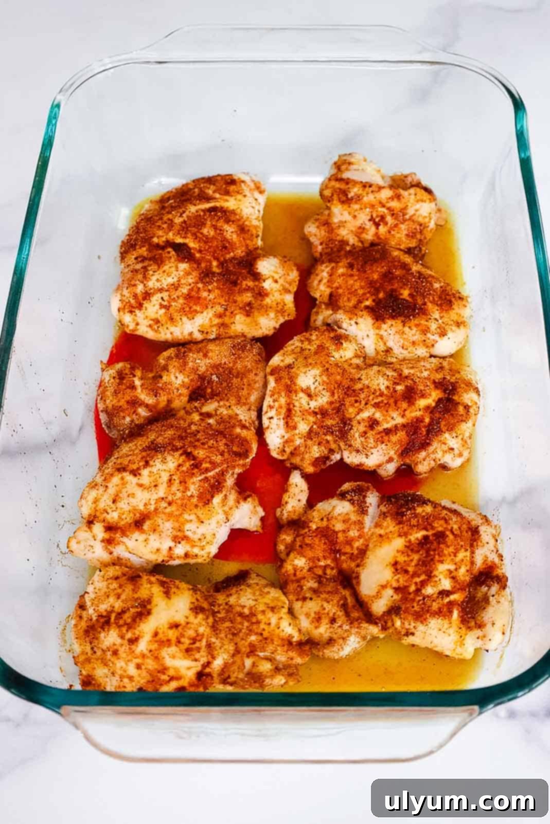 Mouthwatering Oven Baked BBQ Boneless Chicken Thighs 5 Seasoned chicken thighs placed in a glass dish with liquid pooling underneath, ready for the oven.