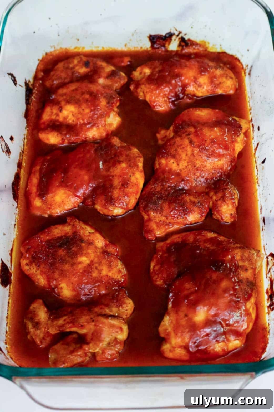 Mouthwatering Oven Baked BBQ Boneless Chicken Thighs 7 Fully cooked oven baked BBQ boneless chicken thighs resting in a glass baking dish, coated in a thick layer of caramelized sauce.