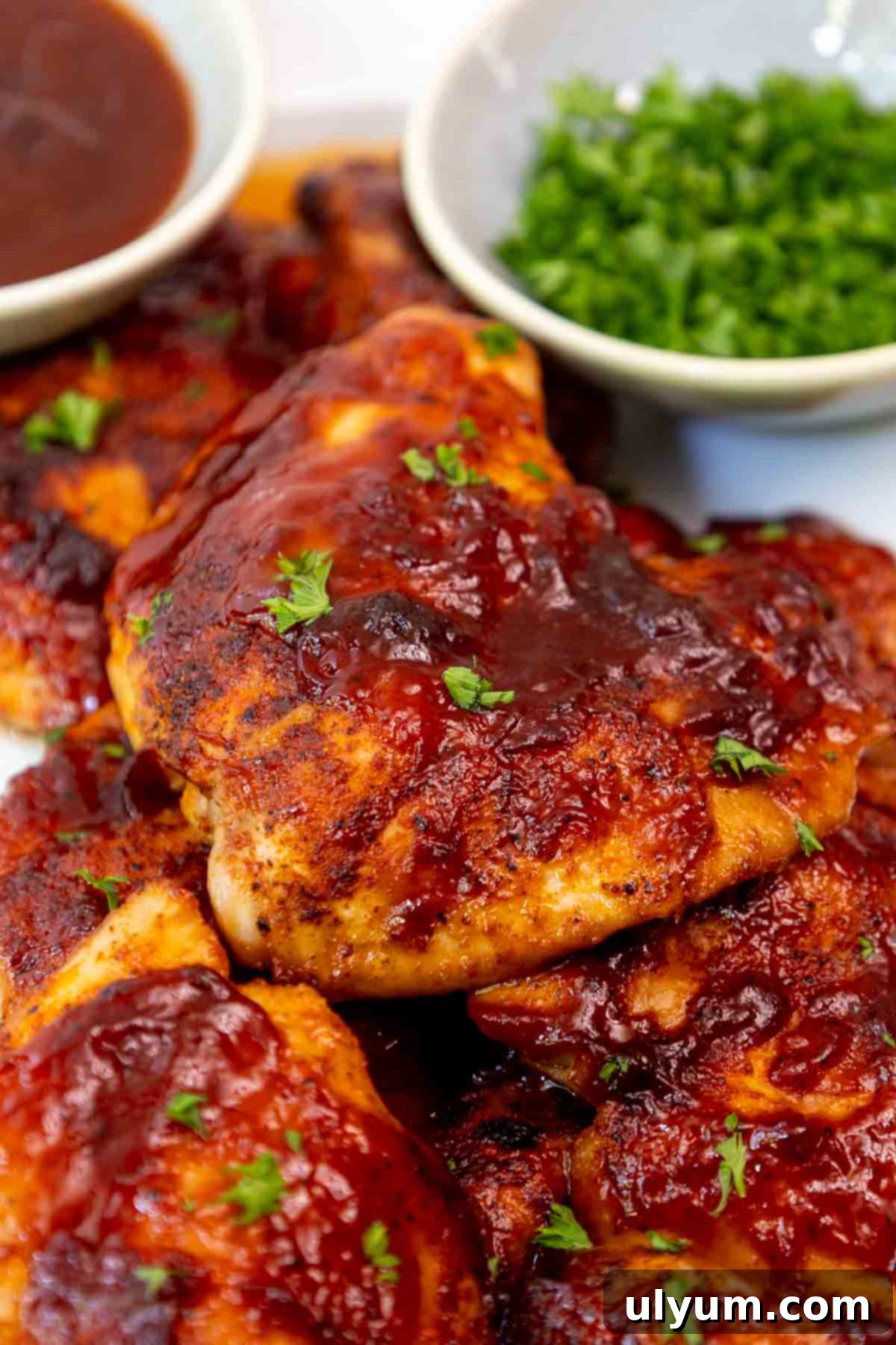 Mouthwatering Oven Baked BBQ Boneless Chicken Thighs 8 Pile of juicy oven baked BBQ boneless chicken thighs on a serving platter garnished with chopped parsley.