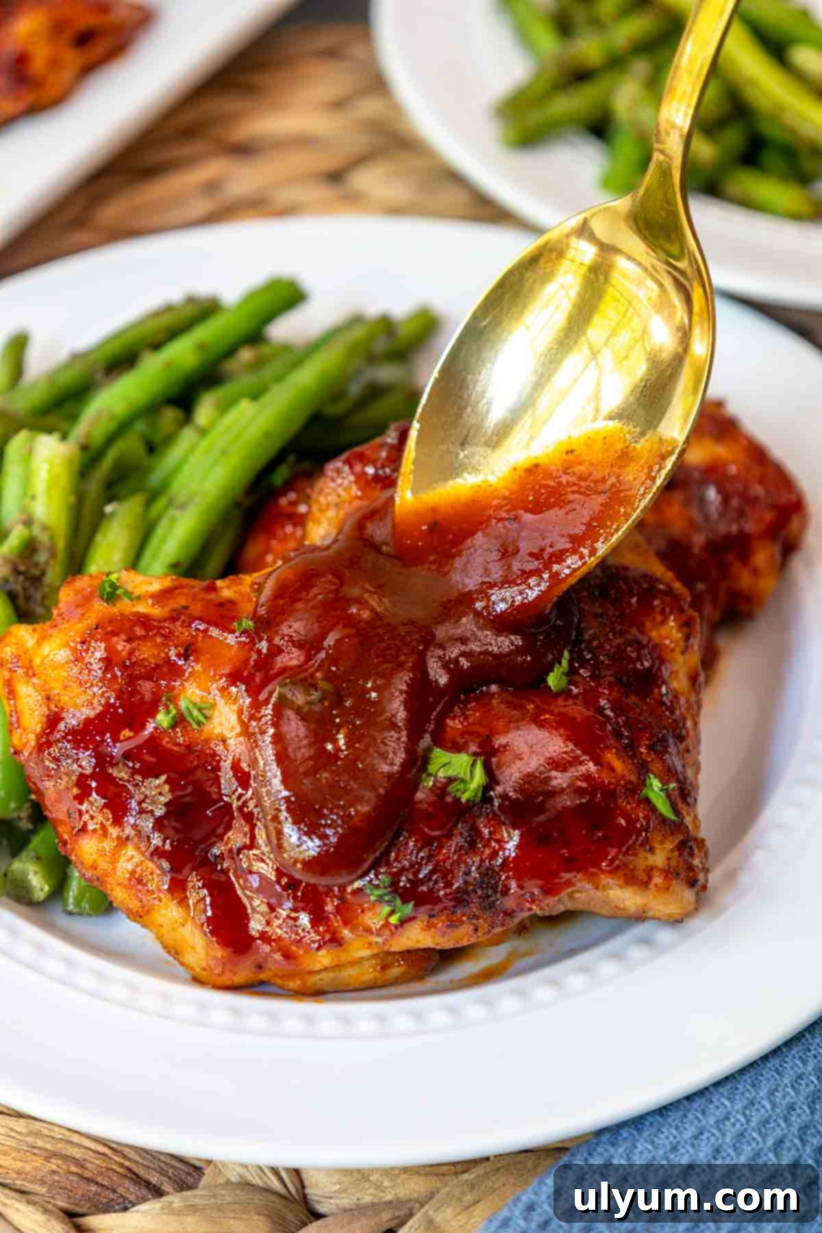 Mouthwatering Oven Baked BBQ Boneless Chicken Thighs 9 Golden spoon drizzling extra BBQ sauce over a serving of baked boneless skinless chicken thighs.