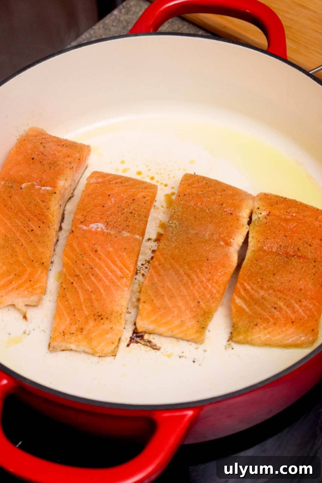 Seasoned salmon fillets placed in a red Dutch oven with oil, beginning to sear and lightly brown on one side.
