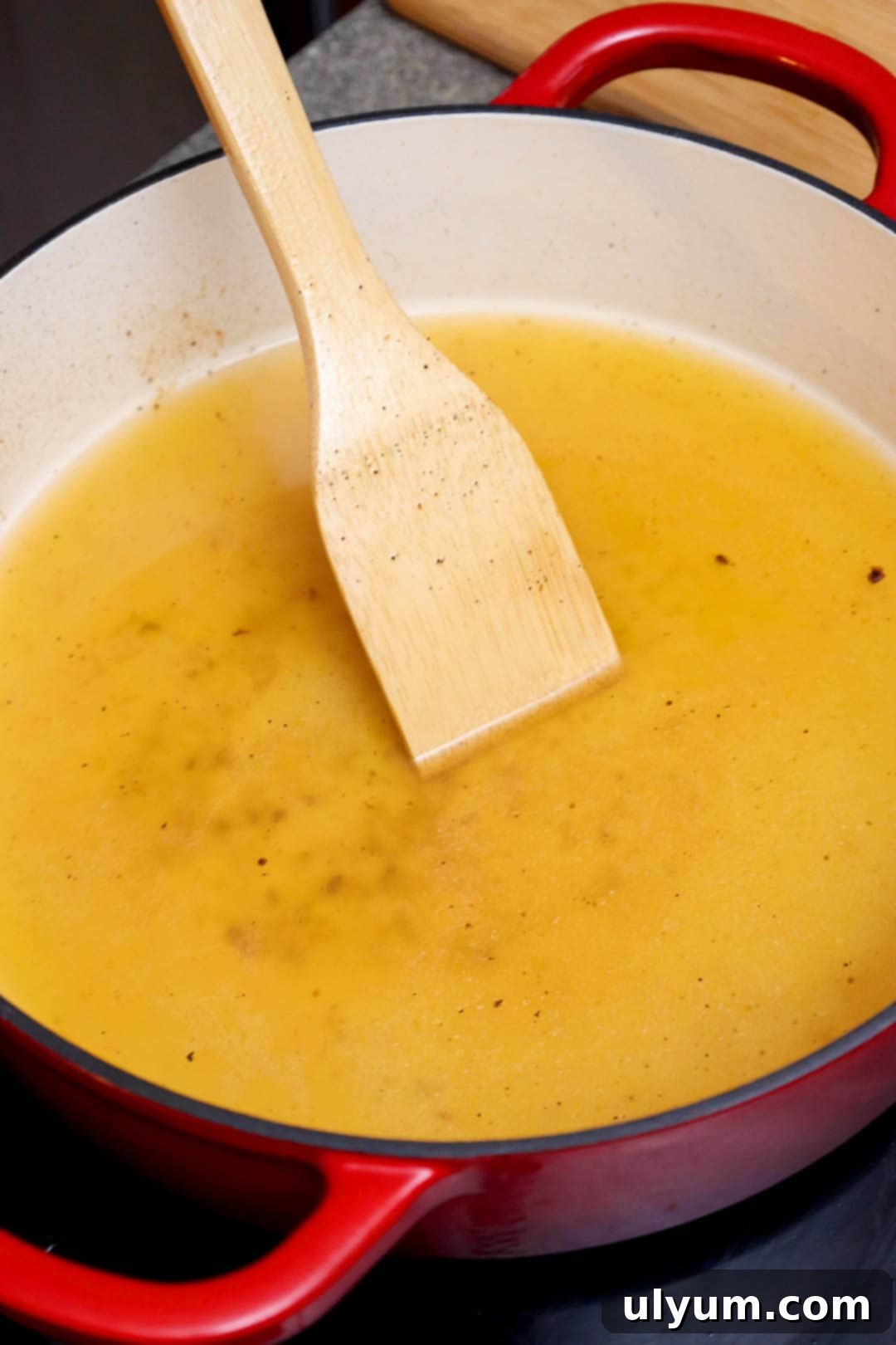 A wooden spoon scraping up the fond from the bottom of the pan fileld with chicken broth.