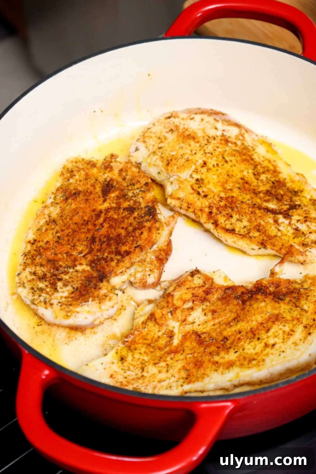 Seasoned chicken breasts searing in olive oil inside a Dutch oven, developing a golden brown crust.