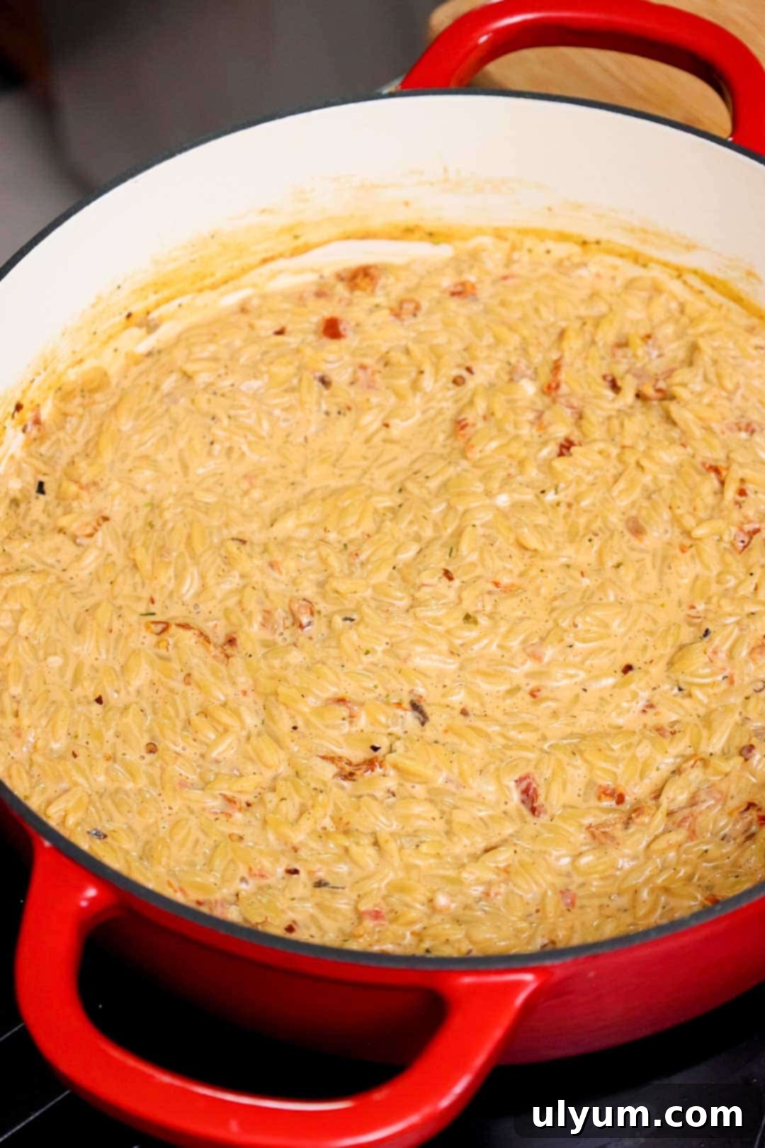 Creamy orzo with visible bits of sun-dried tomato thickening in a Dutch oven.