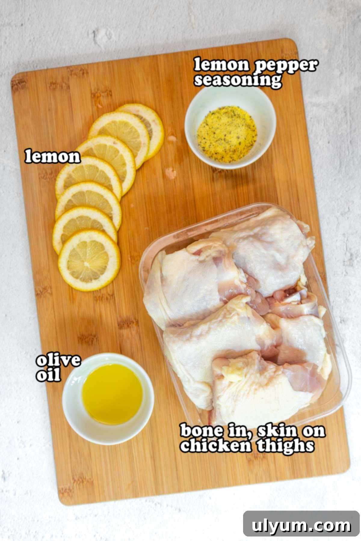 Golden Lemon Pepper Chicken Thighs 3 Ingredients for lemon pepper chicken laid out on a wooden cutting board, including sliced lemons, lemon pepper seasoning, olive oil, and raw chicken thighs with skin and bone.