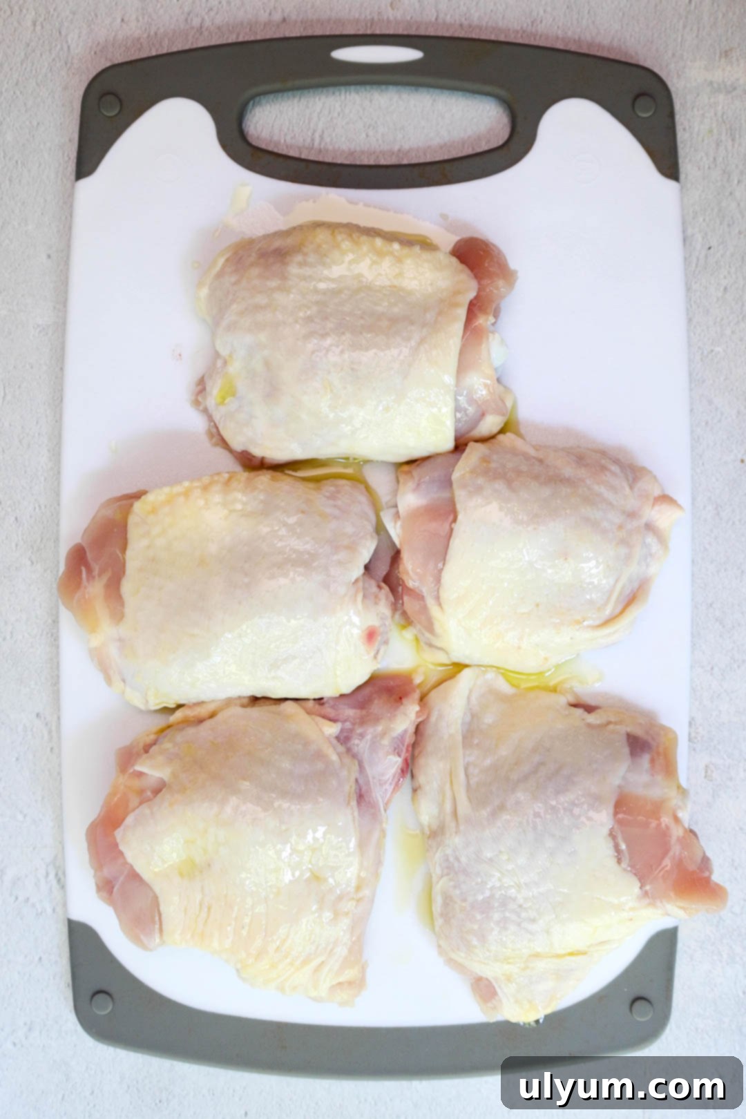 Golden Lemon Pepper Chicken Thighs 5 Five raw chicken thighs drizzled with olive oil placed on a cutting board.